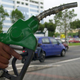 A man holds a gas pump in front of a street scene.